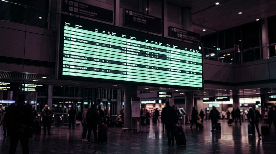Papan jadwal bandara dengan baris waktu menyala hijau lembut di ruangan gelap